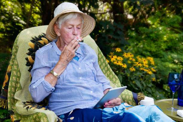 85 years old Senior Woman Relaxing at Home. She is smoking marijuana joint as medicinal cannabis.
The lady wearing a blue dress. She is sit outside near a gazebo. Photo was taken in Quebec Canada.