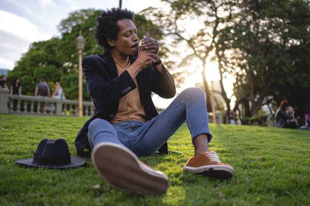 African American man sitting on a grass area and smoking a cigarette